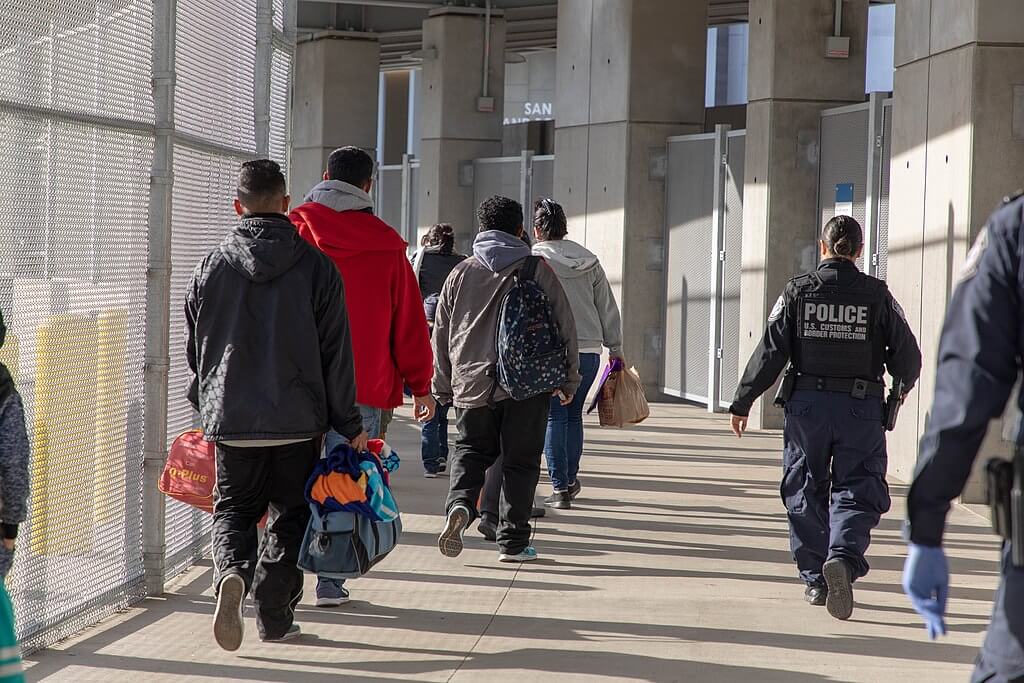 Grupo de migrantes vistos de espalda haciendo fila para solicitar asilo. Los neuvos programas de parole humanitario buscan reducir la cantidad de tráfico humano en la frontera y generar nuevas vías migratorias.